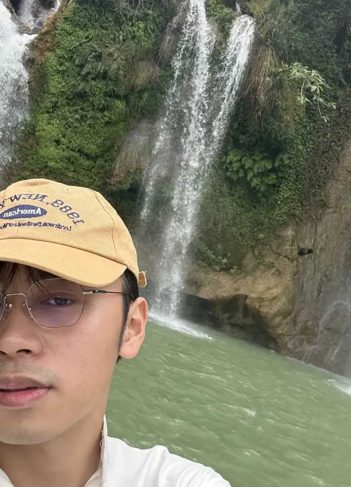 Selfie of Hung in a yellow cap by a waterfall